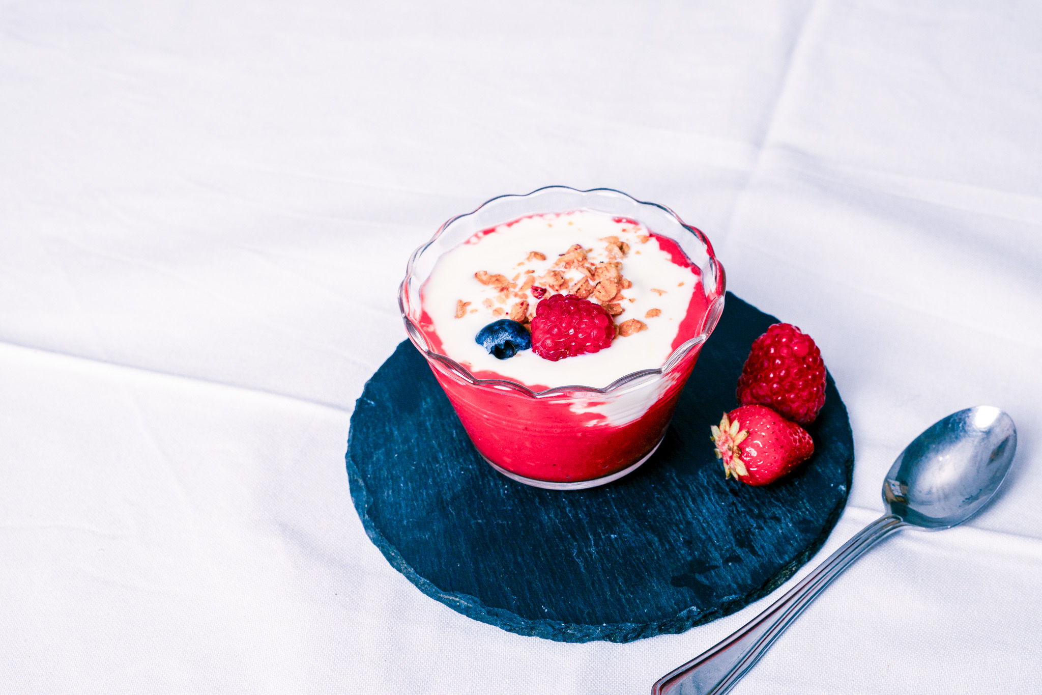 Abbildung von Fruchtige Joghurt-Topfencreme im Glas mit Löffel, Himbeere und Erdbeere