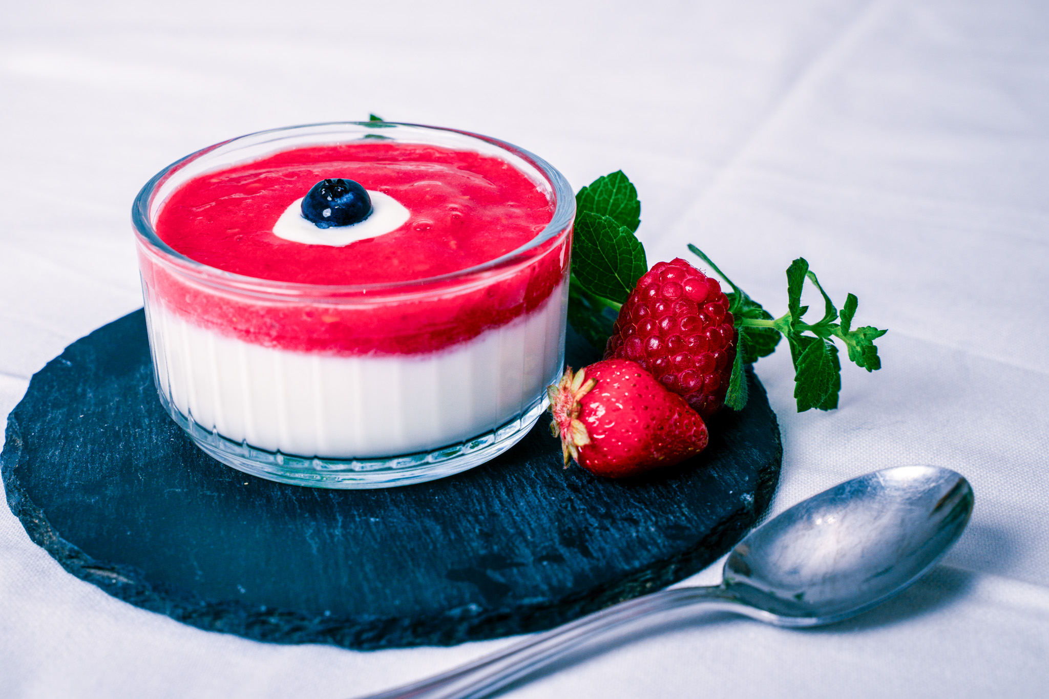 Abbildung von Sommerliche Topfencreme mit Beerenspiegel im Glas mit Löffel, Himbeere und Erdbeere